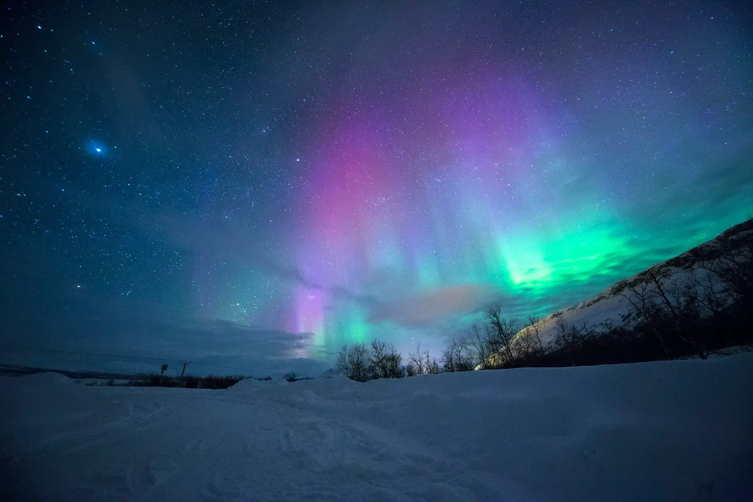 Aurora boreale viola e verde in un cielo stellato sopra un paesaggio innevato
