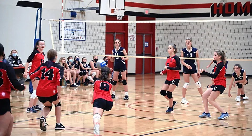 Studentesse della Clearwater Secondary School giocano a pallavolo su un campo da basket con un tabellone segnapunti visibile.