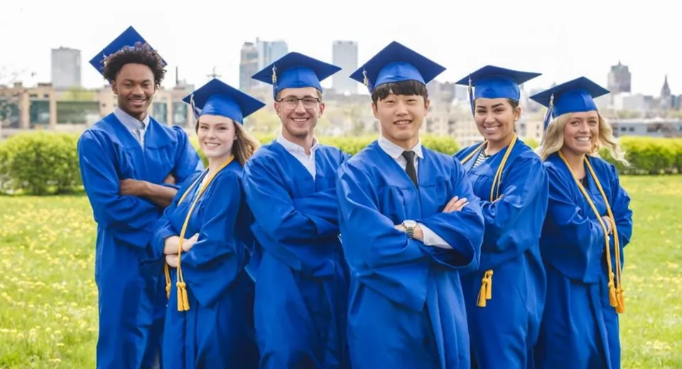I diplomati della Northeastern Wisconsin Lutheran High School in toga blu sono in piedi davanti a uno sfondo urbano.
