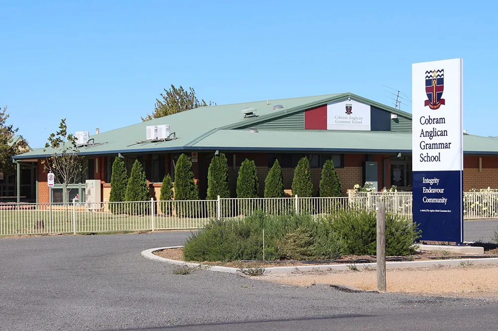 El edificio de una planta de la Cobram Anglican Grammar School con tejado verde y un gran cartel en la entrada.