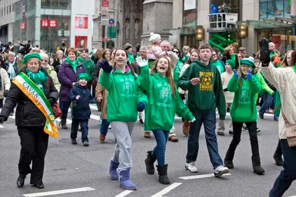 Grupo de jóvenes y adultos vestidos de verde desfilando y saludando en una calle urbana