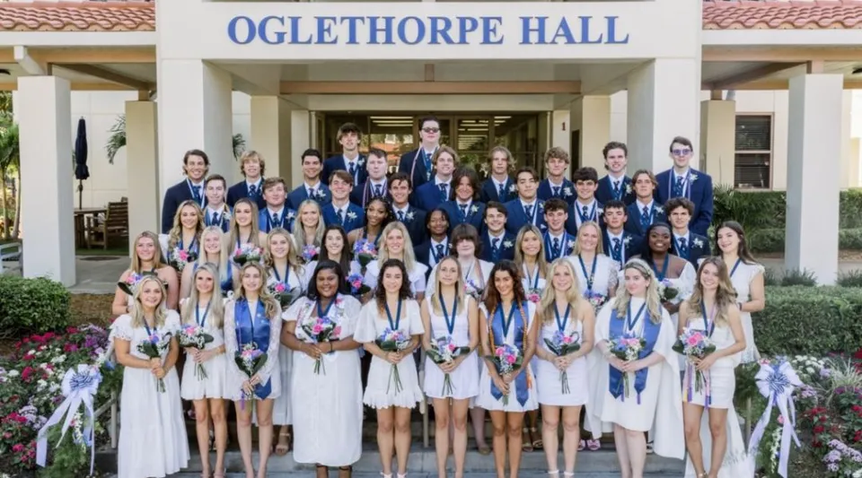 Un grande gruppo di studentesse in toga bianca festeggia il diploma davanti alla Oglethorpe Hall nel campus della Saint Edward's School.