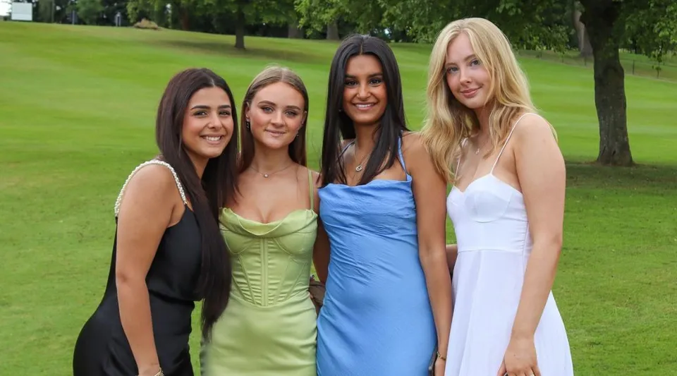 Quattro studentesse della The Mary Erskine School sono in piedi in un parco su un prato davanti agli alberi.