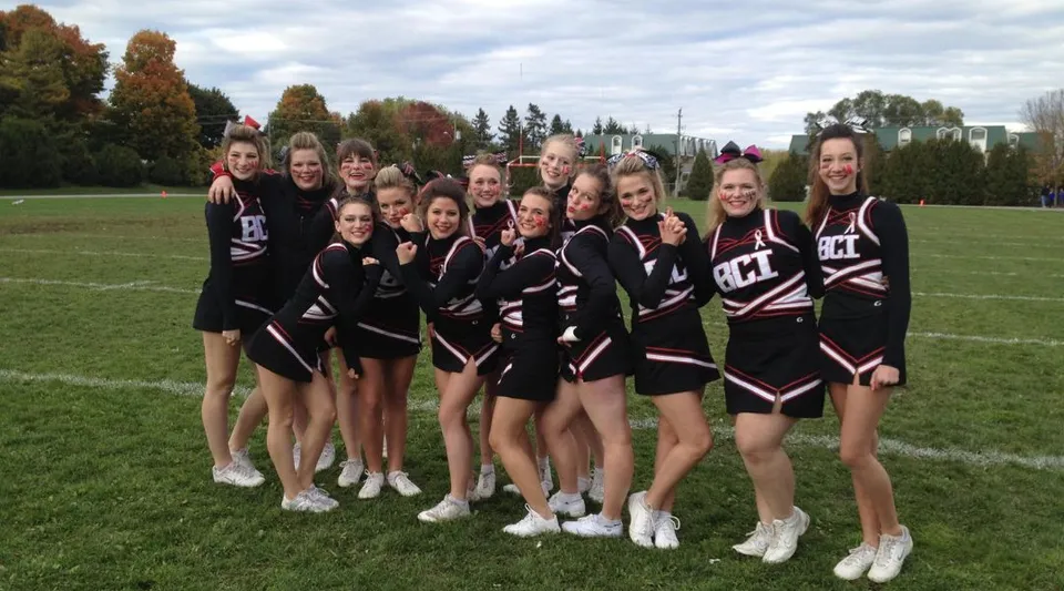 Un gruppo di giovani cheerleader in uniforme nera e bianca si trova sul campo del Brockville Collegiate Institute.