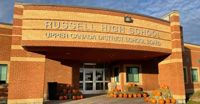 La entrada de Russell High School con un letrero del Upper Canada District School Board y una decoración de calabaza en primer plano.