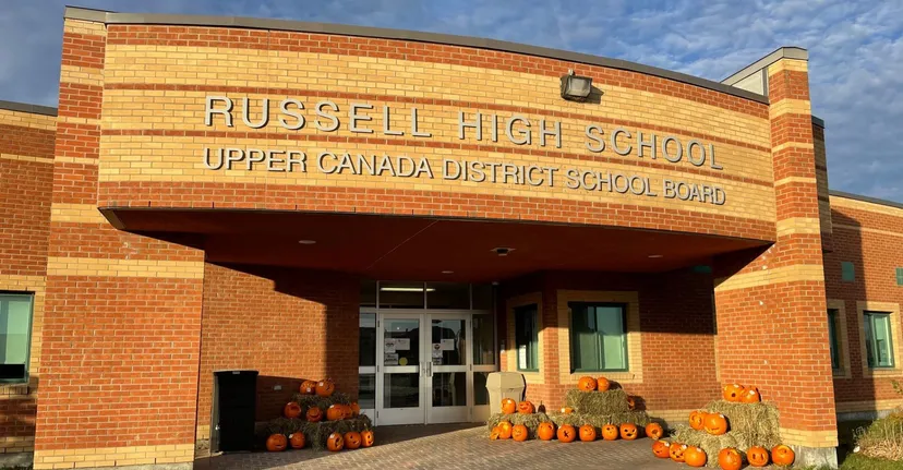 L'ingresso della Russell High School con un cartello dell'Upper Canada District School Board e una decorazione a forma di zucca in primo piano.
