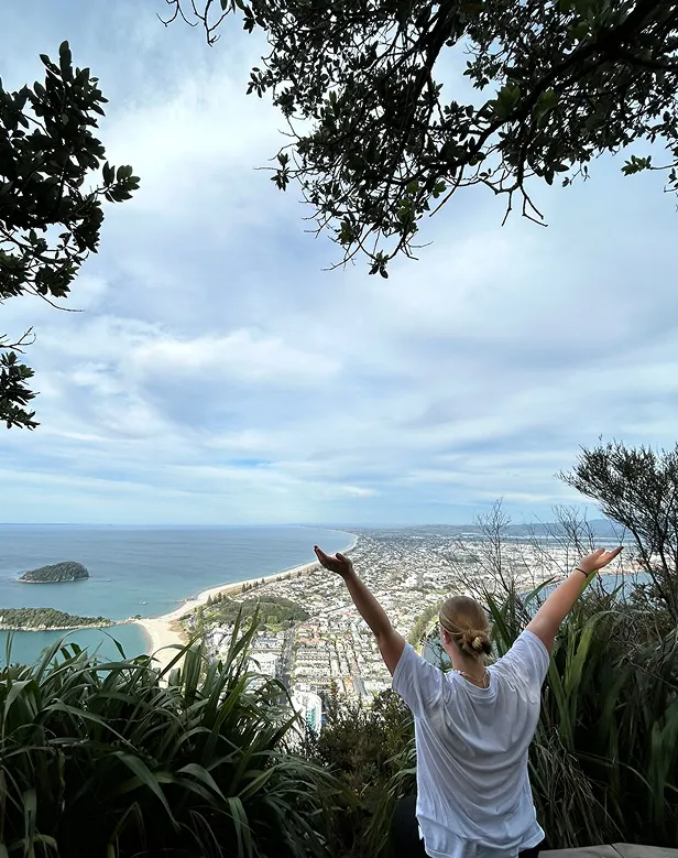 Chica de espaldas con los brazos abiertos en un mirador sobre una ciudad costera y su larga playa