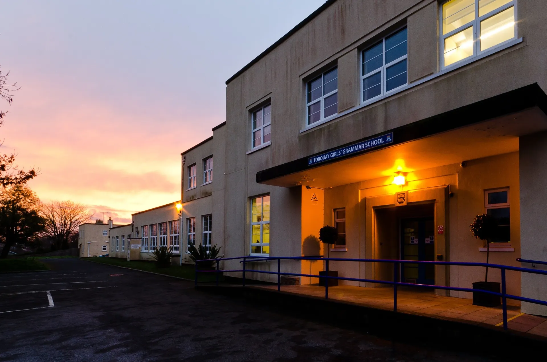 L'edificio a più piani della Torquay Girls Grammar School al tramonto con finestre illuminate e una rampa all'ingresso.