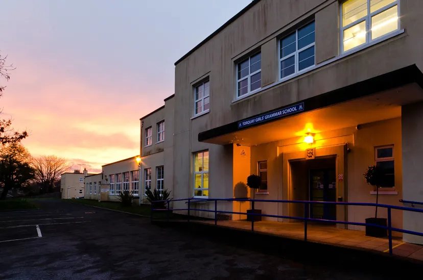 L'edificio a più piani della Torquay Girls Grammar School al tramonto con finestre illuminate e una rampa all'ingresso.