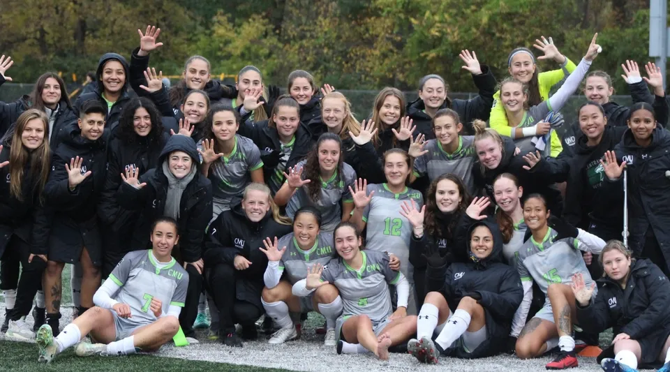 Un gruppo di giovani donne in abbigliamento sportivo saluta all'aperto davanti a uno sfondo boscoso nel campus della Central Methodist University.