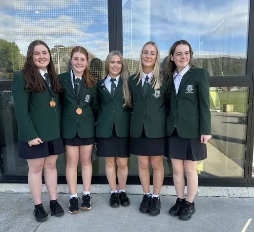 Cinco estudiantes con uniforme escolar verde posan juntas, dos de ellas con medallas