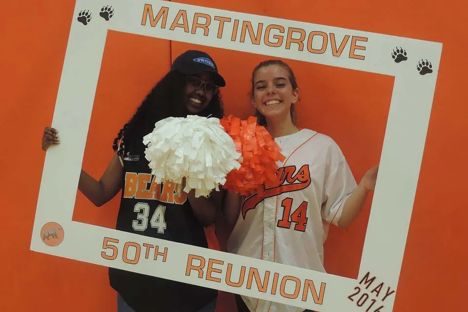 Due persone posano davanti a uno sfondo arancione con un testo sul 50° anniversario del Martingrove Collegiate Institute.