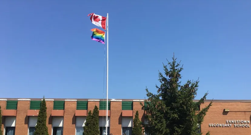 Davanti all'edificio in mattoni della Ernestown Secondary School sventolano una bandiera canadese e una bandiera arcobaleno sul pennone.