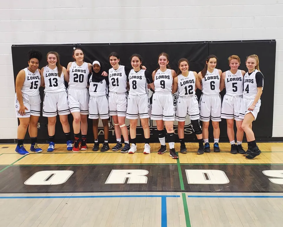 Un gruppo di giovani giocatrici di basket in maglia bianca si trova sul campo da basket della Lord Beaverbrook High School.