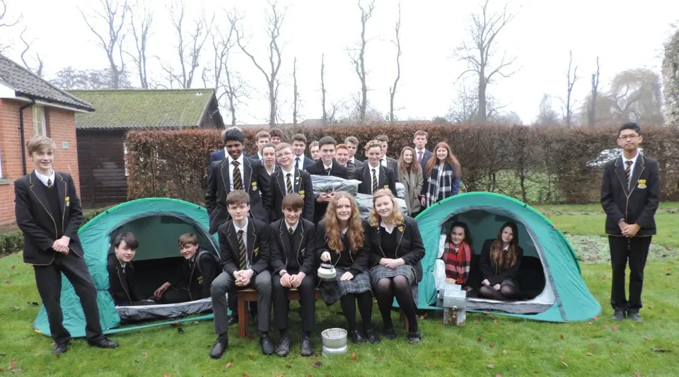 Un gruppo di studenti della Thetford Grammar School posa all'aperto davanti a una casetta in legno e agli alberi.