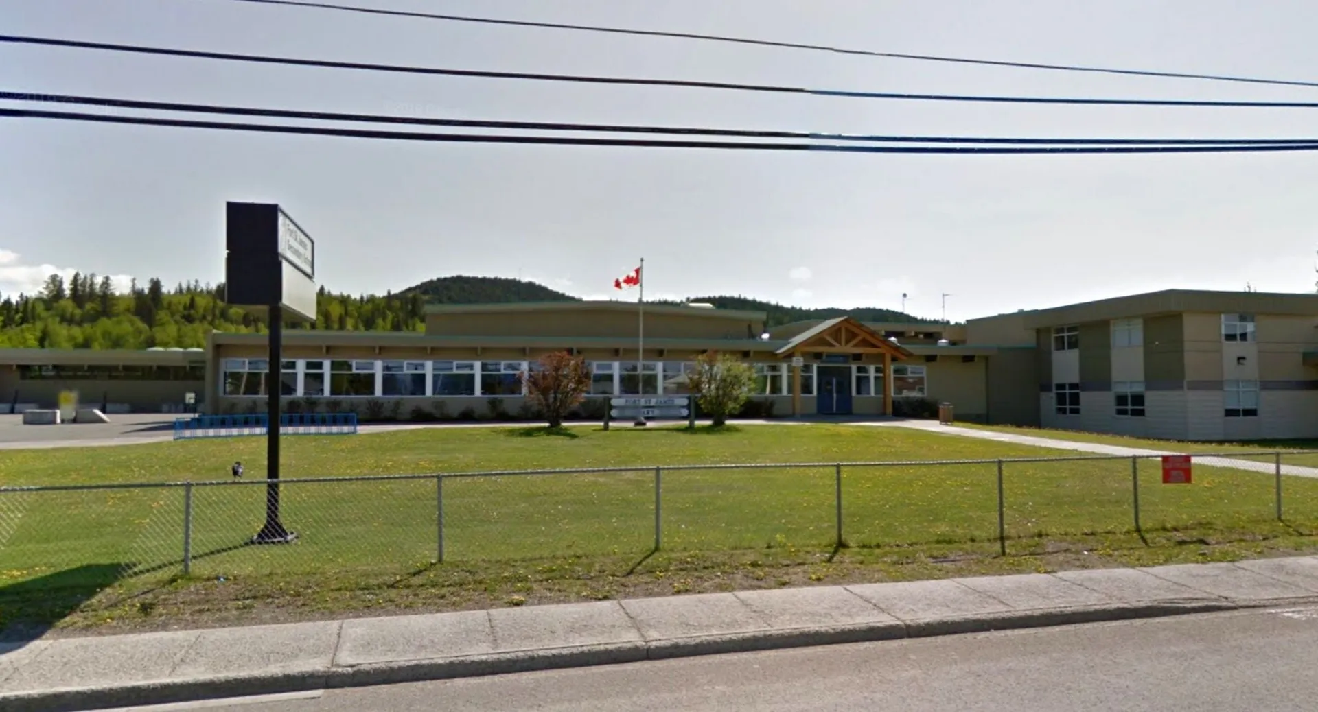 L'edificio scolastico della Fort St. James Secondary con la bandiera canadese sullo sfondo davanti a un prato con recinzione.