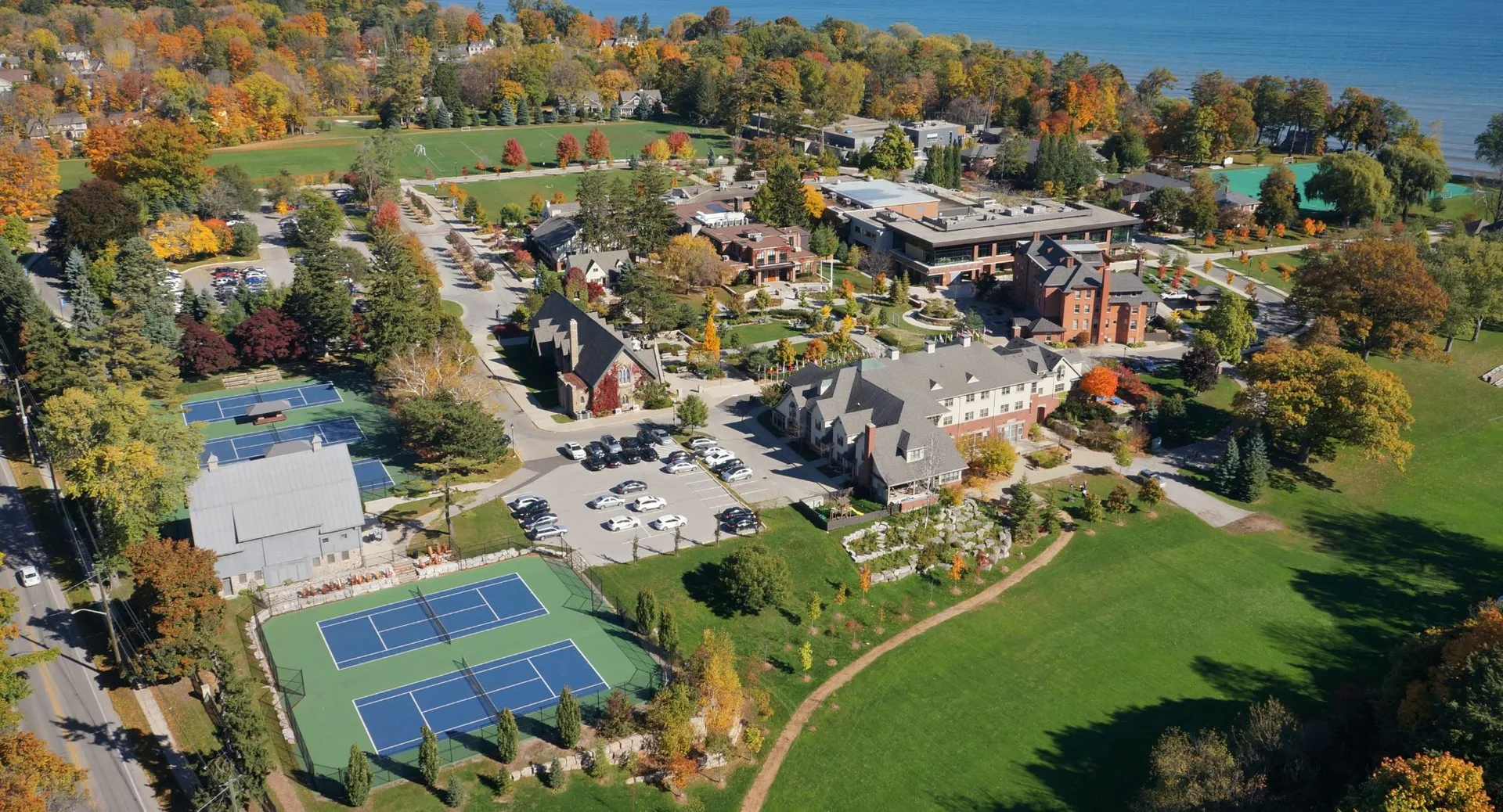 Vista aerea del campus dell'Appleby College con edifici scolastici, campi da tennis e alberi autunnali a bordo lago.
