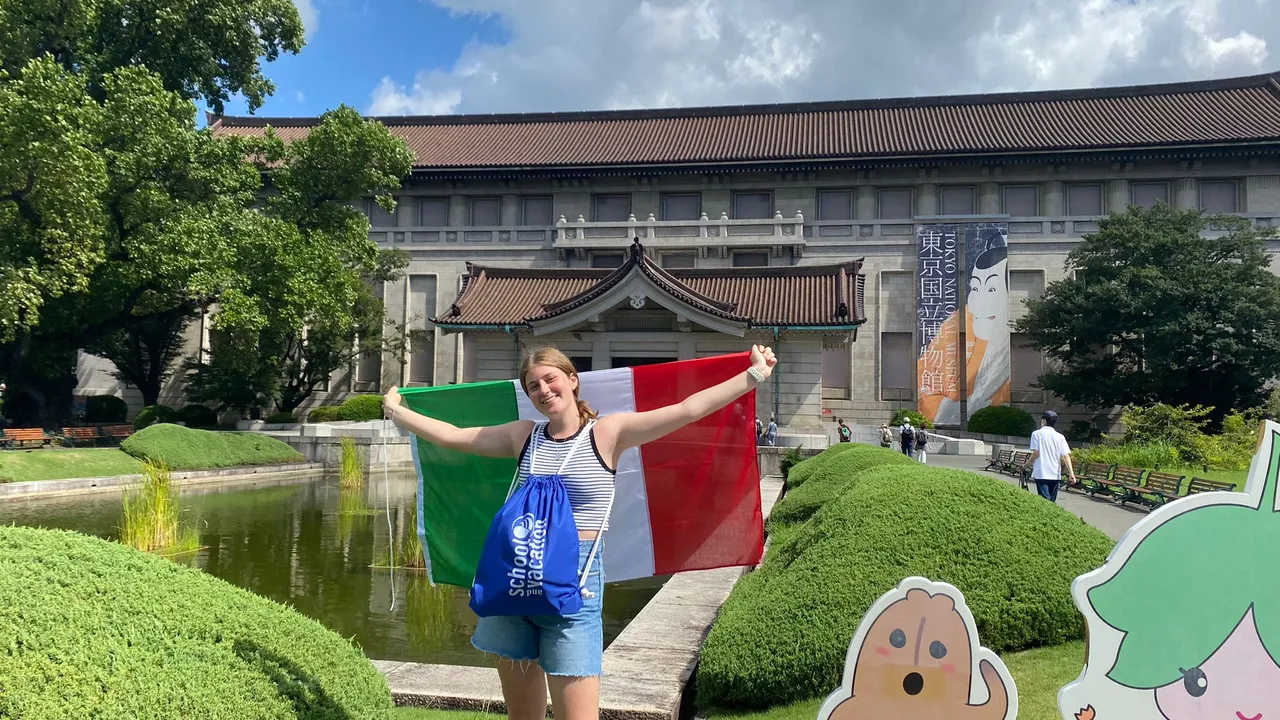 Studentessa in vacanza studio tiene la bandiera italiana davanti a un grande edificio giapponese
