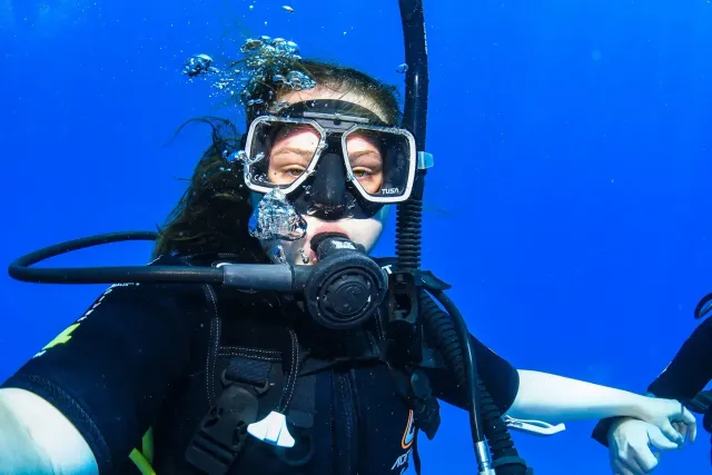 Studentessa in immersione subacquea con maschera ed erogatore in acque blu profonde