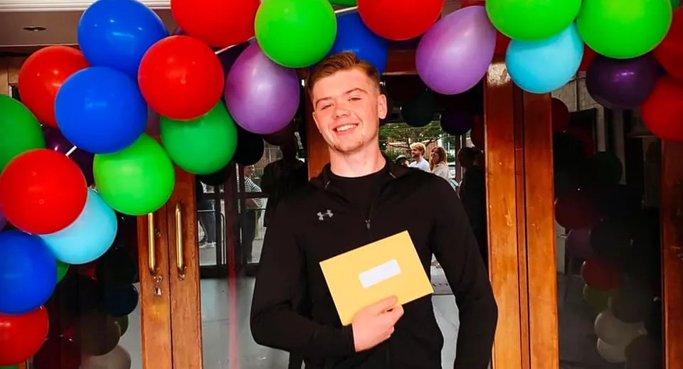 Una persona in maglietta nera è in piedi davanti a un allestimento di palloncini colorati nel campus della Trafalgar School.