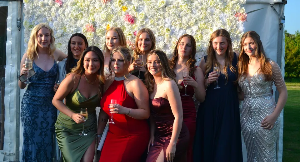 Un gruppo di giovani donne in abito da sera sta davanti a una vivace parete di fiori nel campus della Ashford School.