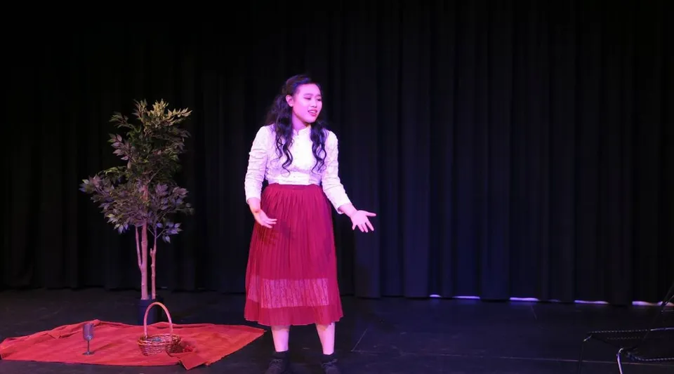 Una studentessa si trova sul palco del Cyril Jackson Senior Campus davanti a un sipario scuro con delle piante davanti.
