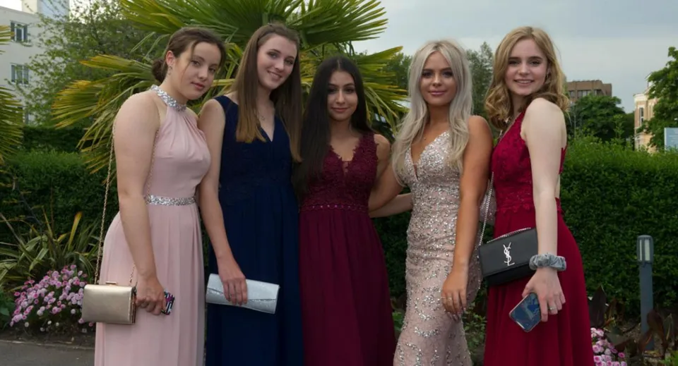 Cinque studentesse della Bournemouth Collegiate School in posa in abito formale davanti a uno sfondo di piante tropicali.