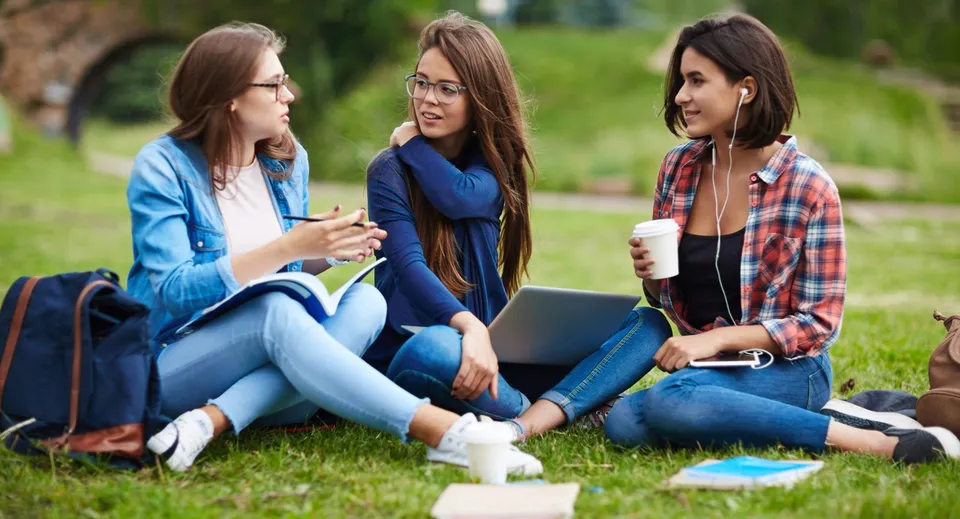 Tre studentesse della Worthgate School Canterbury sono sedute sul prato e chiacchierano davanti a uno sfondo verde.