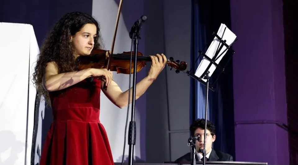 Una studentessa della SEK International School El Castillo suona il violino sul palco indossando un abito rosso.
