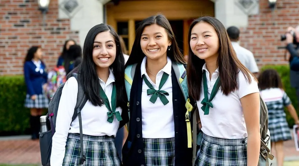 Tre studentesse in divisa scolastica sorridono davanti a un edificio in mattoni delle Annie Wright Schools.