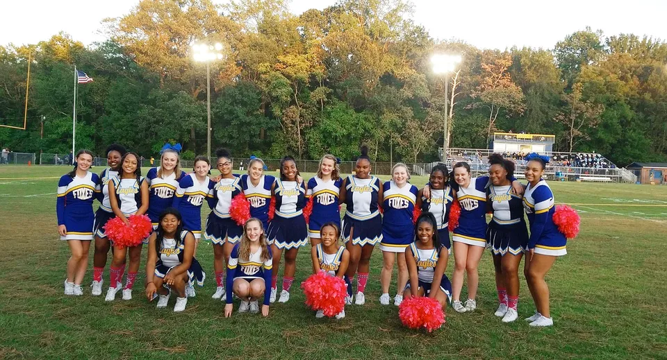 Un gruppo di cheerleader in divise colorate posa insieme sul campo sportivo della King George Secondary School.