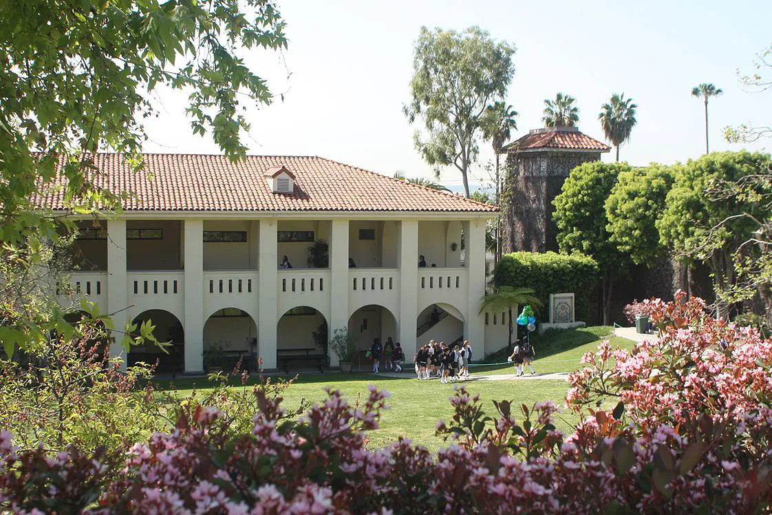 El edificio de la Immaculate Heart Central School con tejado de tejas rojas, arcos y un césped con flores en primer plano.