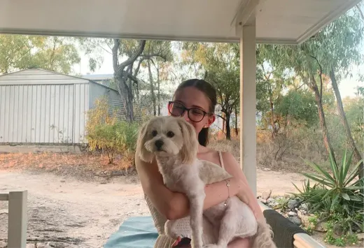 Antonia hält einen kleinen Hund auf einer Veranda in australischer Landschaft im Arm