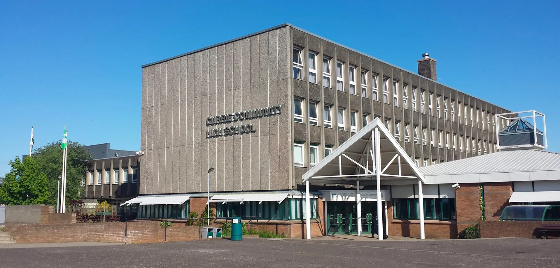 L'edificio principale moderno della Currie Community High School con un'area pavimentata adiacente e spazi verdi sullo sfondo.