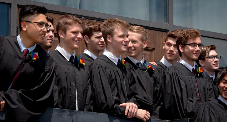 Un gruppo di studenti della St. John’s-Kilmarnock School in abito da diploma davanti a un edificio scolastico.