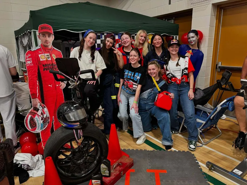 Un gruppo di studentesse della Memorial Composite High School posa accanto a una decorazione a tema automobilistico.