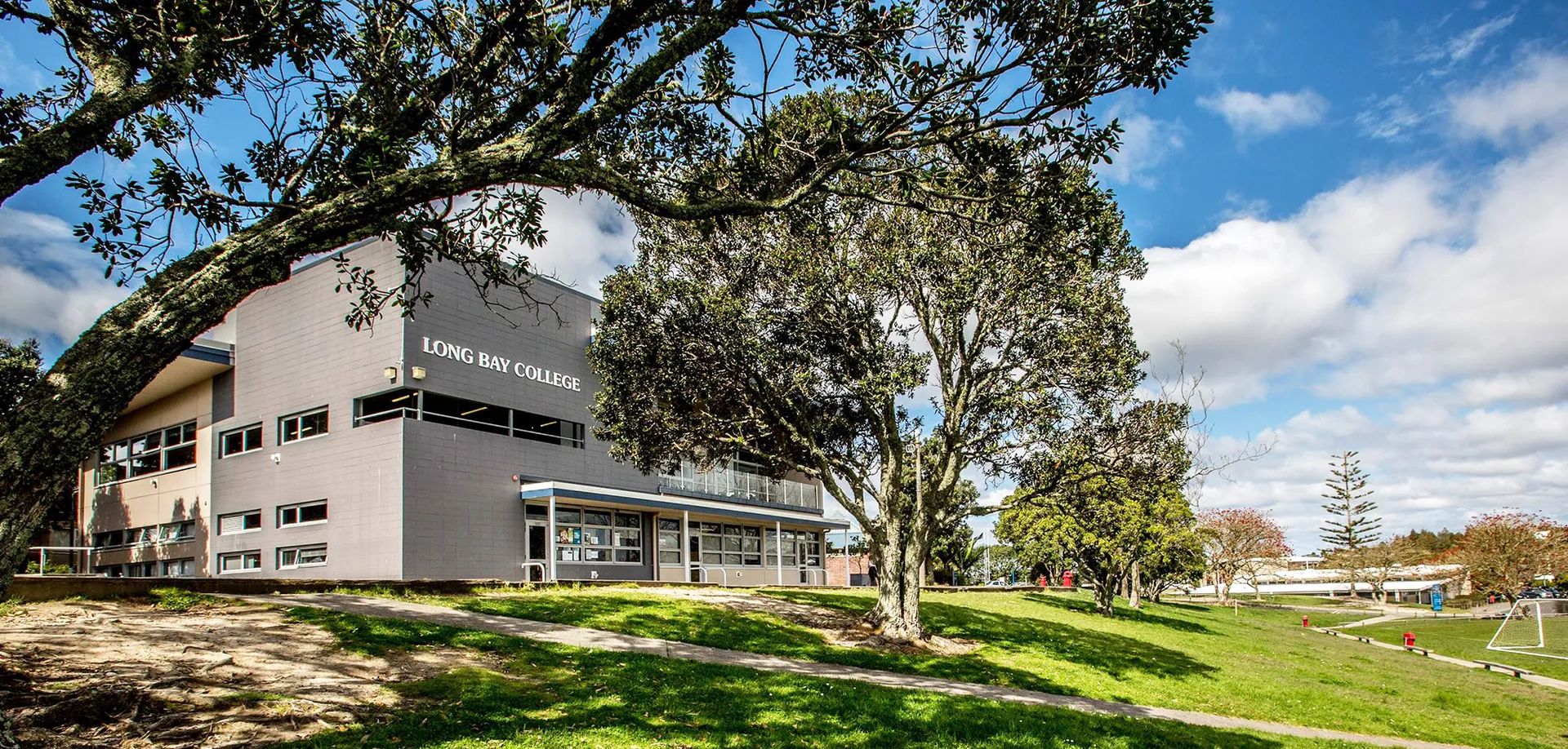 Il moderno edificio grigio del Long Bay College è circondato da un paesaggio verde e alberi.
