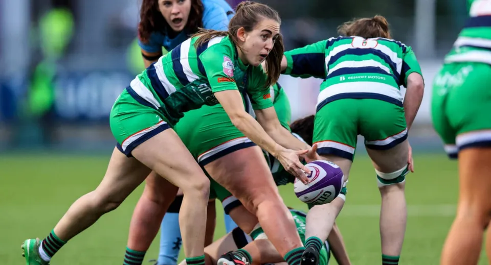 Un gruppo di giocatrici di rugby in divisa verde e bianca durante una scrum sul campo da gioco del Fingal Community College.