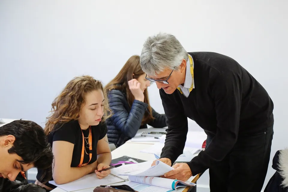 Un gruppo di persone, tra cui studenti e studentesse e un signore anziano in abito, conversano a un tavolo nel campus di The Sheffield College.
