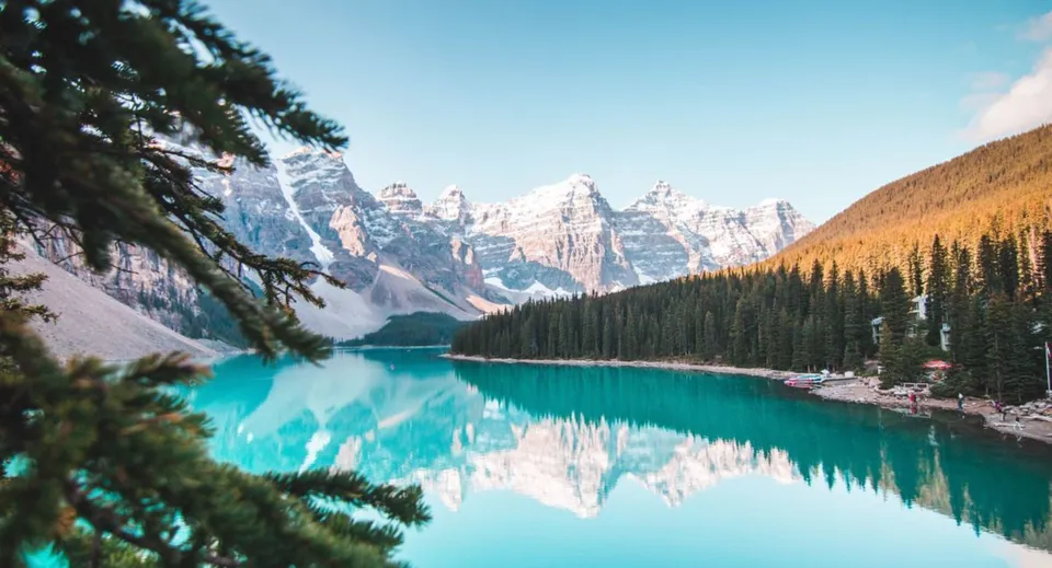 Un lago di montagna turchese in Canada riflette cime innevate e una foresta di conifere.