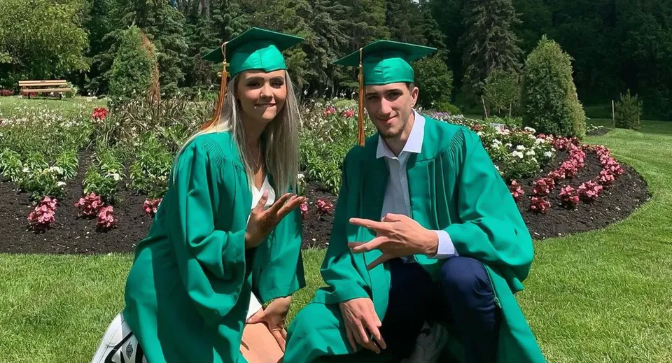 Due studenti con le toghe verdi da diploma si trovano nel giardino del campus del Miles Macdonell Collegiate.