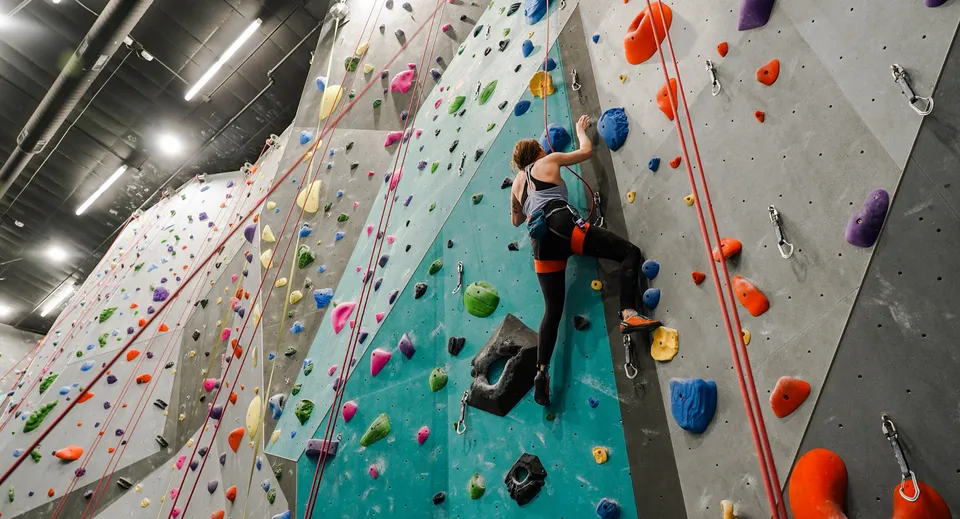 Una persona si arrampica sulla parete colorata nella struttura per arrampicata indoor del Mercy College.