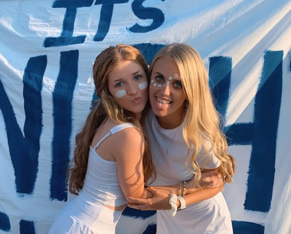 Due studentesse della Central Catholic Jr.-Sr. High School si abbracciano davanti a uno sfondo astratto blu e bianco.