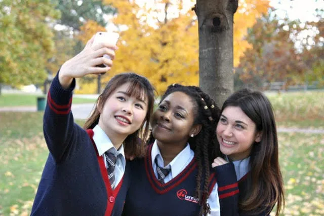 Tres alumnas de la London International Academy se hacen un selfie en el parque con un fondo de follaje otoñal.