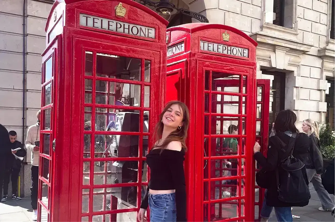 Studentessa sorridente davanti alle cabine telefoniche rosse di Londra