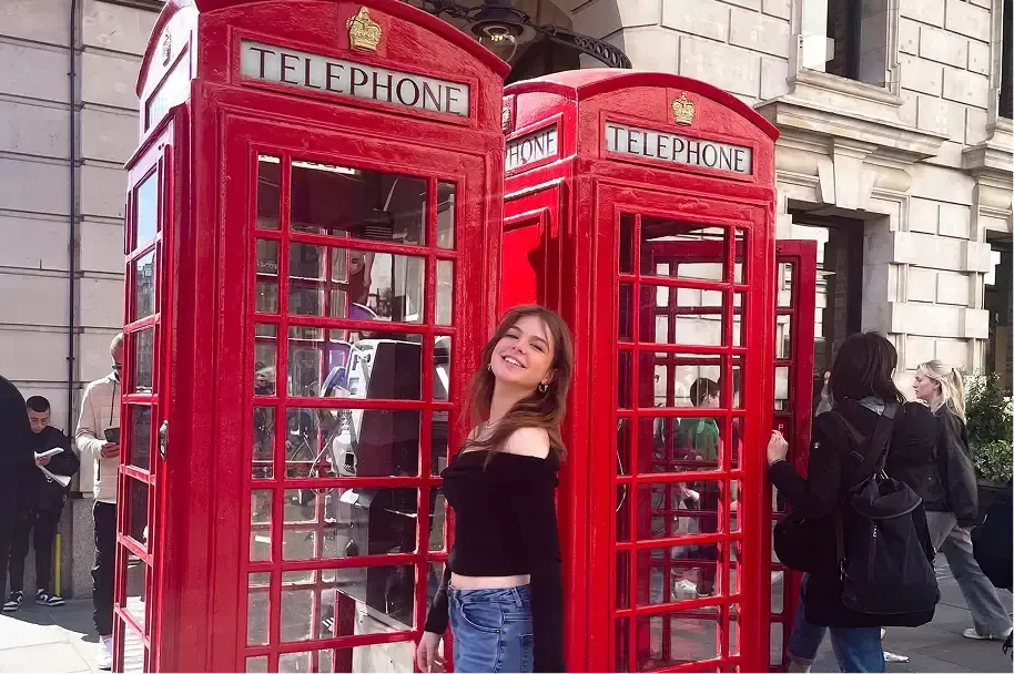 Studentessa sorridente davanti alle cabine telefoniche rosse di Londra