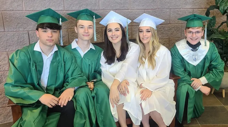 Un gruppo di cinque diplomati in toga verde posa davanti a una parete in mattoni della Charles Finney School.