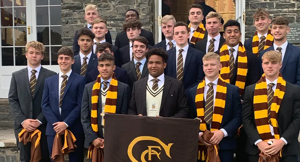 Un gruppo di studenti della Sedbergh School posa davanti a un edificio scolastico in pietra indossando le divise scolastiche con completi e sciarpe a strisce.