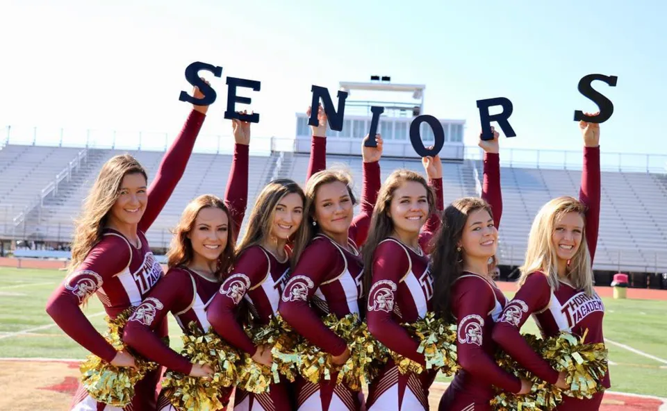 Le cheerleader della Thornton Academy posano sul campo sportivo tenendo in alto le lettere della parola SENIORS.