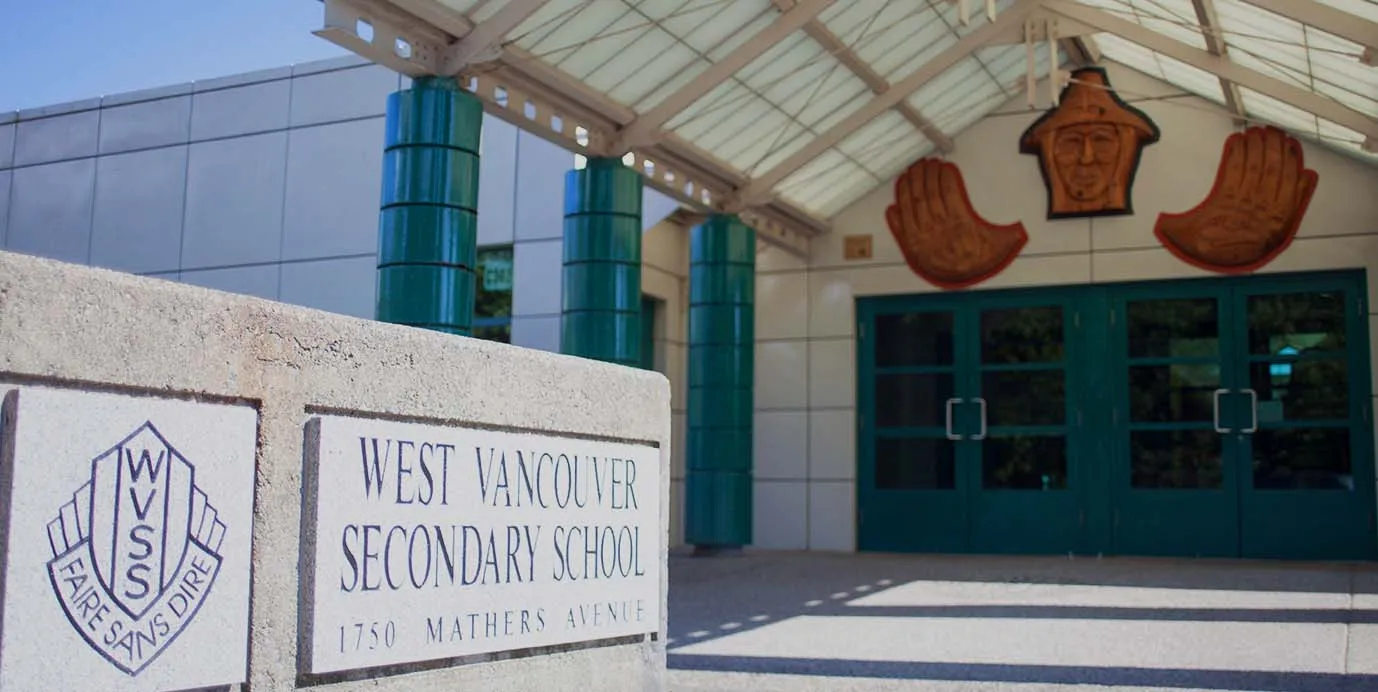El edificio escolar de la West Vancouver Secondary School con un tejado distintivo y grandes ventanas está rodeado por un cartel con el nombre de la escuela y la dirección.